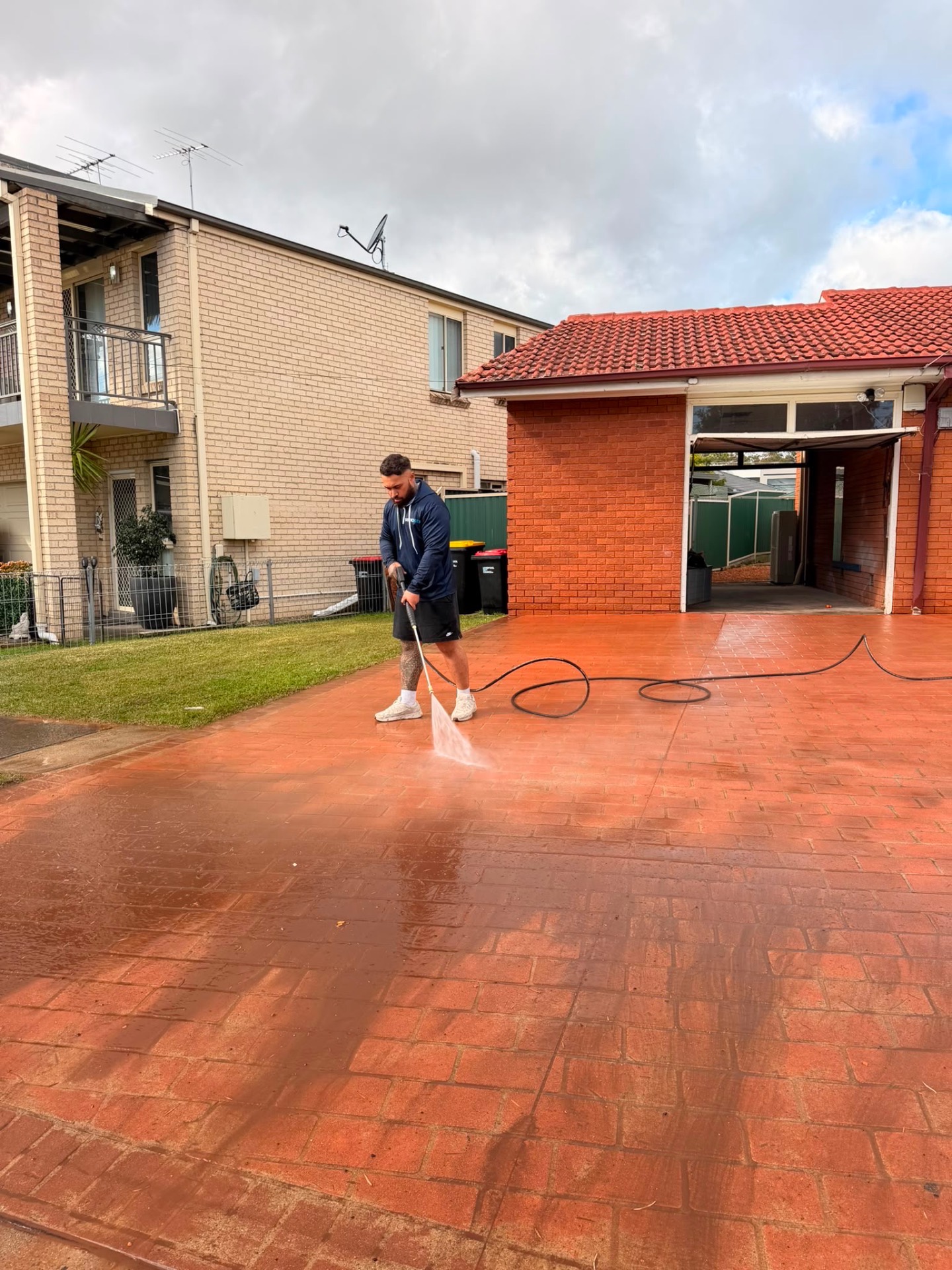 GroundKeep pressure washing a red paver driveway mid-wash, Sydney